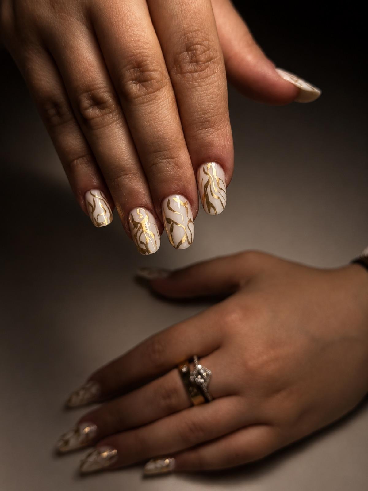 Long white nails with marbled swirls and fine gold detail, hand-painted at Empire nail salon in Corby
